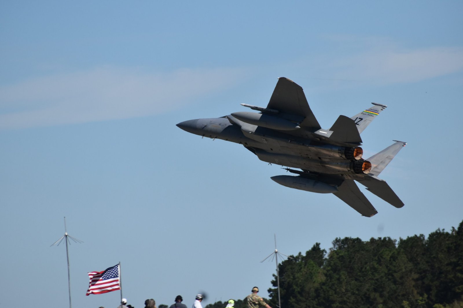 F-15 Eagle in flight with afterburners, American flag visible below, airshow