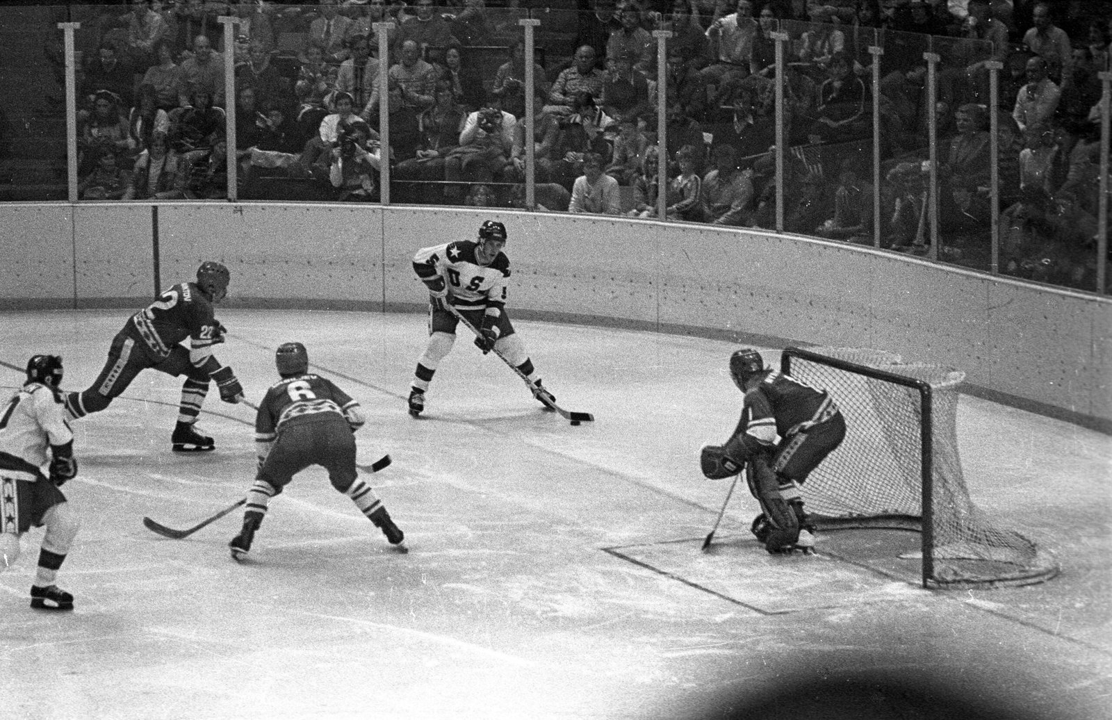 Action photograph from the 1980 Winter Olympics hockey game between the United States and the Soviet Union. Several players cluster along the boards while competing for control of the puck inside a packed indoor arena. The scene captures close physical play and intensity, reflecting direct athletic competition during a moment widely associated with Cold War rivalry.