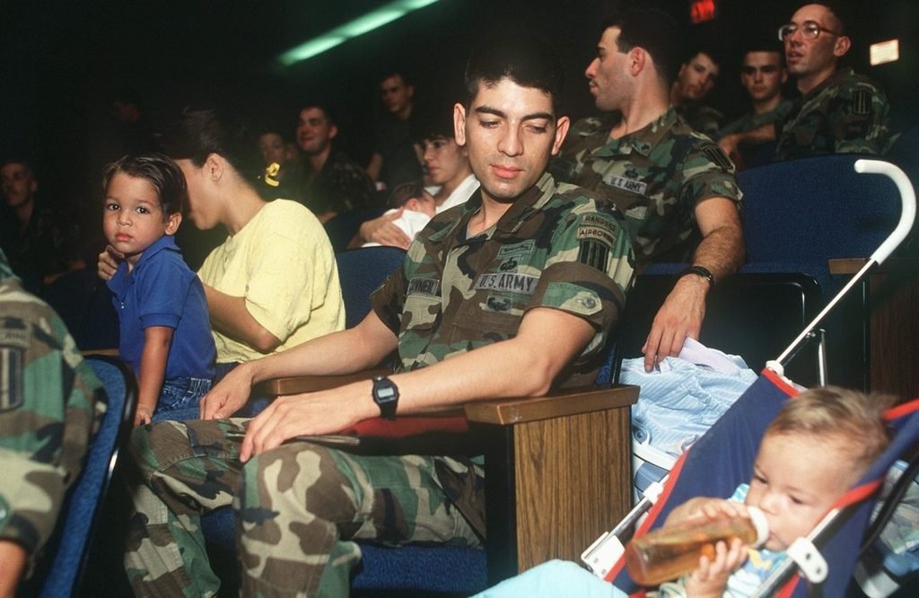 U.S. Army soldiers and their families seated in an auditorium, one soldier with his young son beside him.
